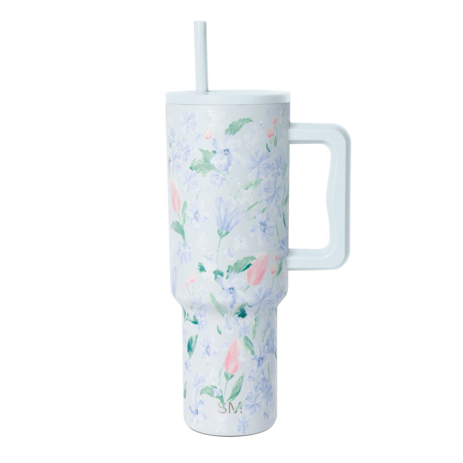 White insulated tumbler with periwinkle, lavender, and pink floral pattern, matching handle and straw, photographed against white background.